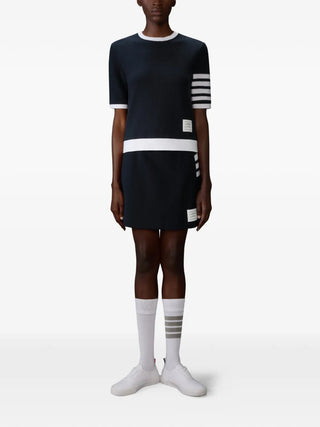 Thom Browne navy cotton box-pleat mini skirt with textured piqué, 4-bar detail and label appliqué, ideal with shirts or knitwear. Available at our Lisbon store