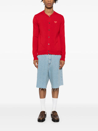Comme Des Garçons PLAY red cardigan in 100% wool. Features a signature heart patch, ribbed V-neck, and long sleeves for a classic finish. 