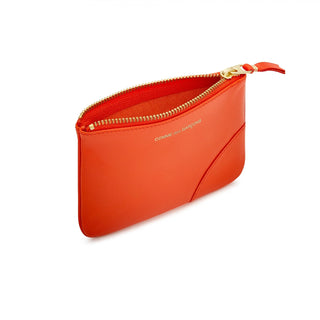 COMME DES GARÇONS WALLET vibrant orange leather wallet. Smooth calfskin, zip-around closure, and gold-tone logo print. Available at our Lisbon store. 