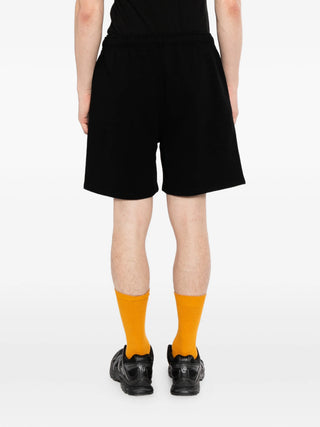 Person wearing black shorts by Canada Goose and orange socks on a white background