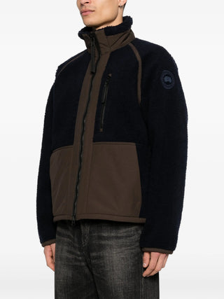 Person wearing a Navy and Brown Jacket with the Canada Goose logo on visible on the sleeve.
