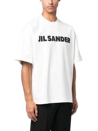 Person wearing a white t-shirt with 'Jil Sander' logo with black pants