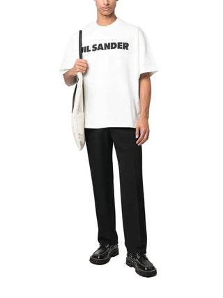 Person wearing a white t-shirt with Jil Sander logo, black pants, and black shoes 