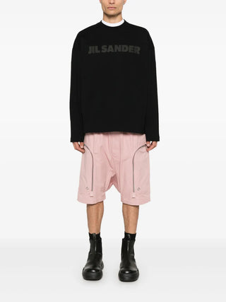 Person wearing a black sweater with 'Jil Sander' branding, pink pants, and black boots.