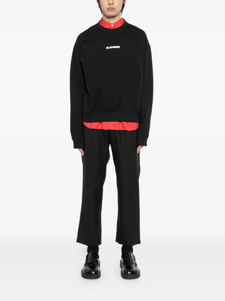 Person wearing a black sweatshirt by Jil Sander over a red shirt with black pants and matching black shoes