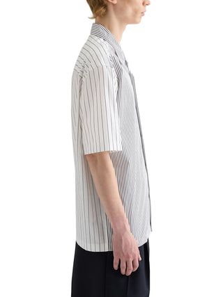 Person wearing a white shirt with black vertical stripes by Jil Sander with black pants. 