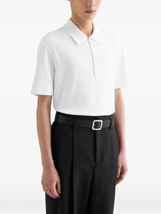 Person wearing a white polo shirt by Jil Sander and black pants with a belt.