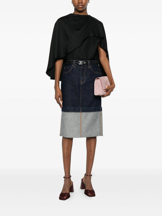 Person wearing a black top with the Khaite Kilian denim skirt with a pink clutch