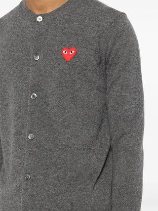 The cardigan by Comme des Garçons. Key details include, front button fastening, long sleeves, and round (crew) neck with the distictive heart patch logo