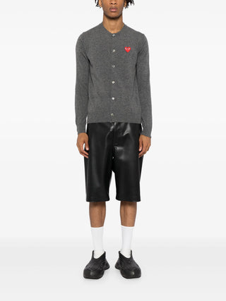 The cardigan by Comme des Garçons. Key details include, front button fastening, long sleeves, and round (crew) neck with the distictive heart patch logo