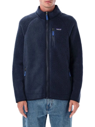 Person wearing a navy fleece jacket with a brand logo by Patagonia with jeans
