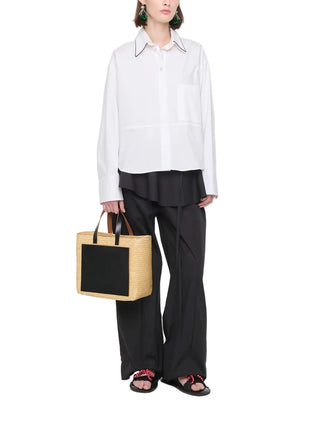 Person wearing a white shirt and black pants holding a black and beige bag 
