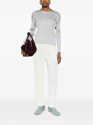 Person wearing the Pleats Please ssey Miyake Montly colours top in Grey styled with white pants and blue shoes. 