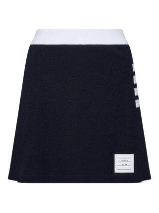Thom Browne navy cotton box-pleat mini skirt with textured piqué, 4-bar detail and label appliqué, ideal with shirts or knitwear. Available at our Lisbon store