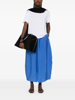 Person wearing a white top and blue skirt holding a black bag by Toteme