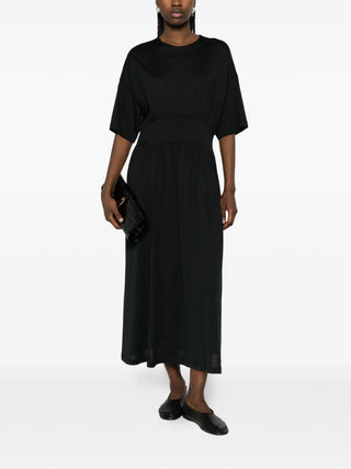 Person wearing a black dress with black shoes and clutch bag by Toteme