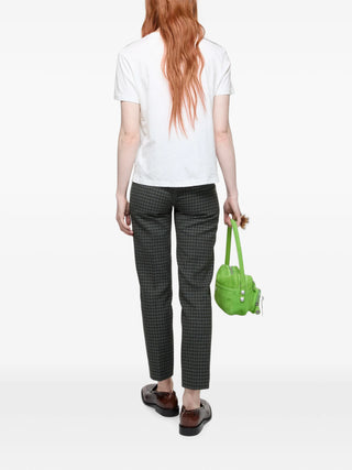Person wearing a white shirt and black checkered pants holding a green handbag 