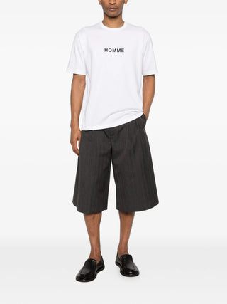 Person wearing a white t-shirt with 'HOMME' text and black shorts