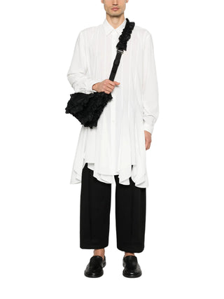 Person wearing a white shirt and black pants holding a black bag with fur trim 