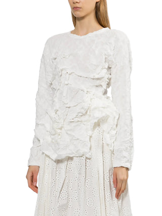 Woman wearing a white long sleeve ruffled top and with a white skirt