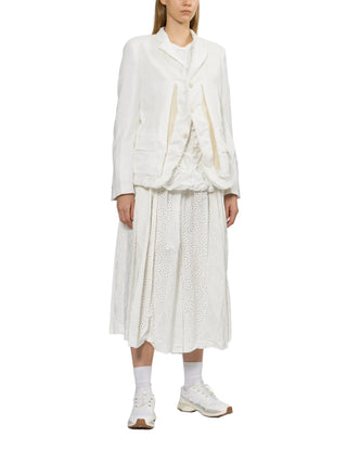 Person wearing a white top under a white jacket with a white skirt and swhite sneakers. 