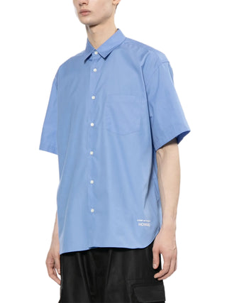 Person wearing a light blue short sleeve shirt with a brand logo by Comme des Garcons