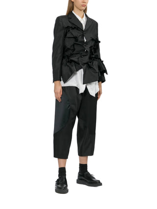Person wearing a black ruffled jacket with black pants and black shoes