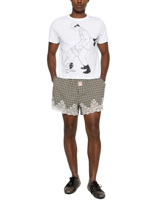 Person wearing a white t-shirt with a graphic design and checkered shorts 