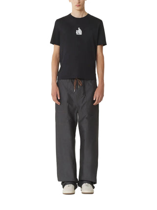 Person wearing a black t-shirt with a small white logo and gray pants
