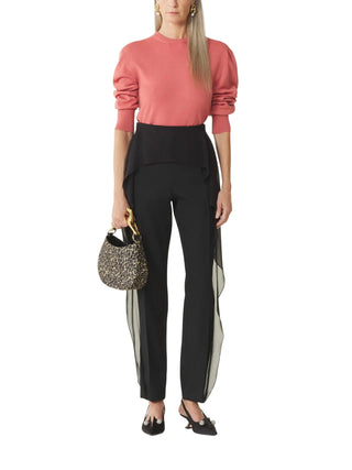 Woman wearing a coral top and black pants holding a glittery handbag 