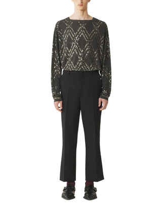 Person wearing a black and gold patterned top with black pants