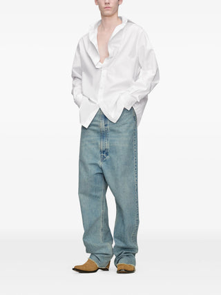 Person wearing an oversized white shirt and light blue jeans with dropped rise by Maison Margiela