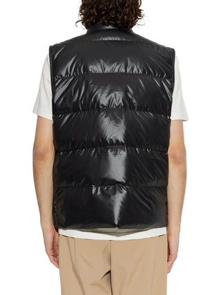 Person wearing a black puffer vest over a white shirt and beige pants