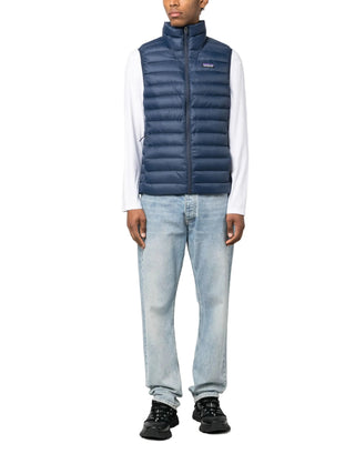 Person wearing a blue puffer vest by Patagonia, light blue jeans, and black shoes 