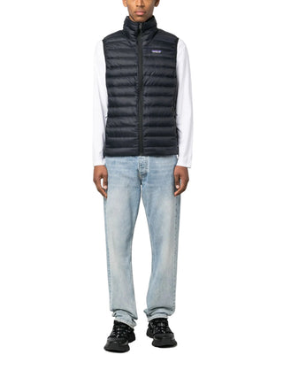 Person wearing a black puffer gilet, white shirt, light blue jeans and black shoes.