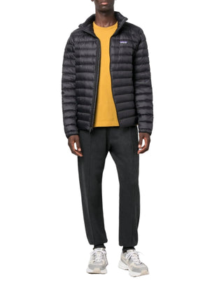 Person wearing a black puffer jacket by Patagonia, yellow shirt, and dark pants with white sneakers