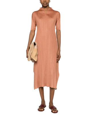 Brown pleated short sleeve midi dress worn by woman with brown sandals and beige tote. 