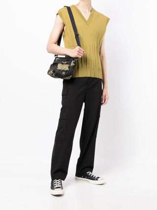 Person wearing a mustard yellow sleeveless top and black pants, holding a camouflage bag by Porter-Yoshida and Co. 