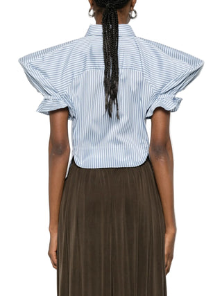 Person wearing a blue and white striped shirt with ruffled sleeves and a brown trousers