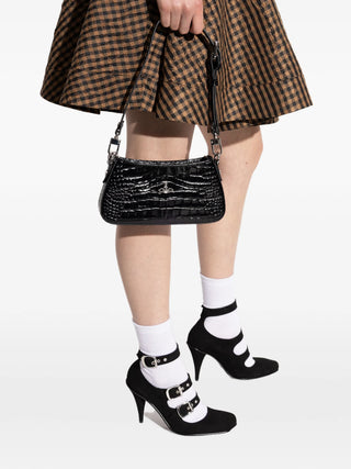 Person wearing a checkered skirt, black high-heeled shoes with buckles, and holding a black handbag 
